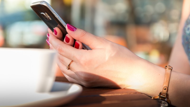 Två kvinnohänder med  rött nagellack håller i en smart telefon
