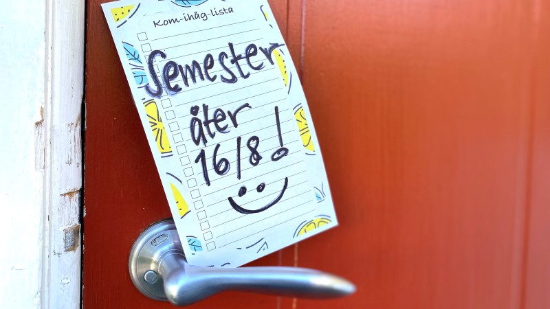 På en röd dörr hänger en lapp med texten: Semester, åter 16 augusti och en glad smiley.