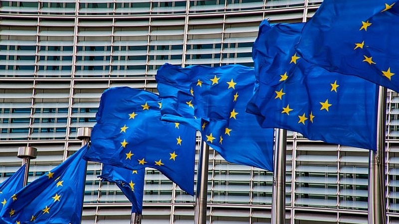 EU-flaggor vajar i vinden framför en fasad med persienner i stål.