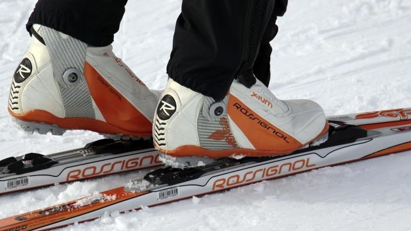 Närbild på ett par fötter i bindningarna på längdskidor. Pjäxorna är orange och vita, liksom skidorna, av märket Rossignol.