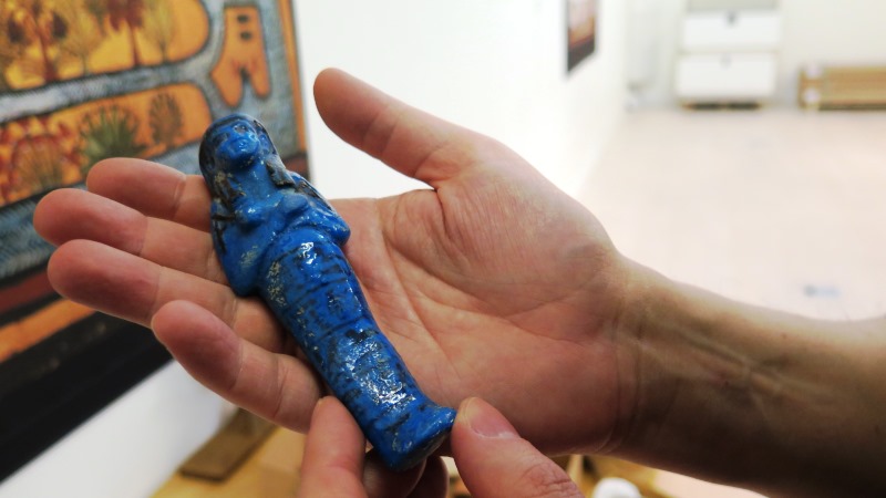 Hand som håller liten blå egyptisk statyett.