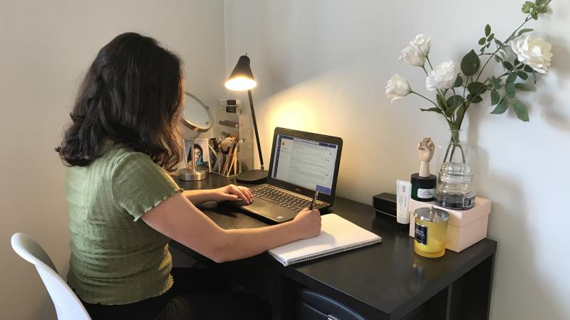 Ung kvinna med mörkt hår sitter vid skrivbord, tittar på en laptop