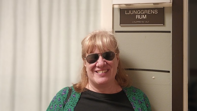En blond leende kvinna med mörka glasögon står under en skylt med texten ”Ljunggrens rum”.