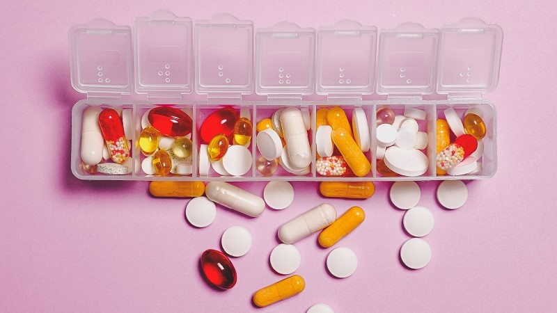 En genomskinlig vit plastlåda med sju fack som är öppna, inuti finns tabletter i olika färg och form. Vita, gula och röda, mot en rosa bakgrund.