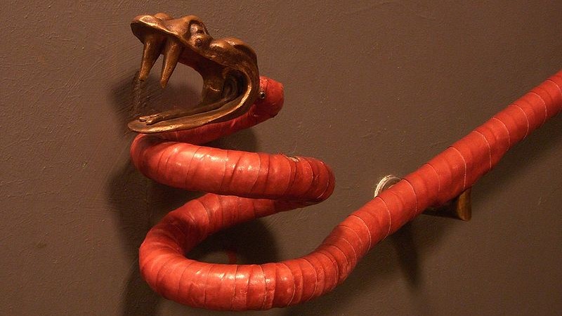 Ett trappräcke format som en orm i bronsfärgad metall lindat med rött läder .