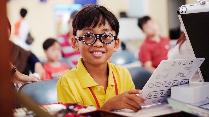 En mörkhyad pojke i gul tröja och testglasögon sitter i skolbänk.