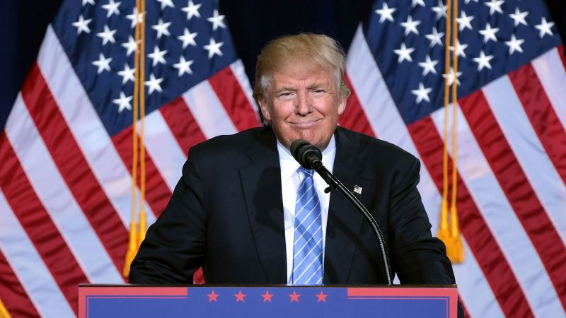 Donald Trump i talarstolen framför amerikanska flaggor.