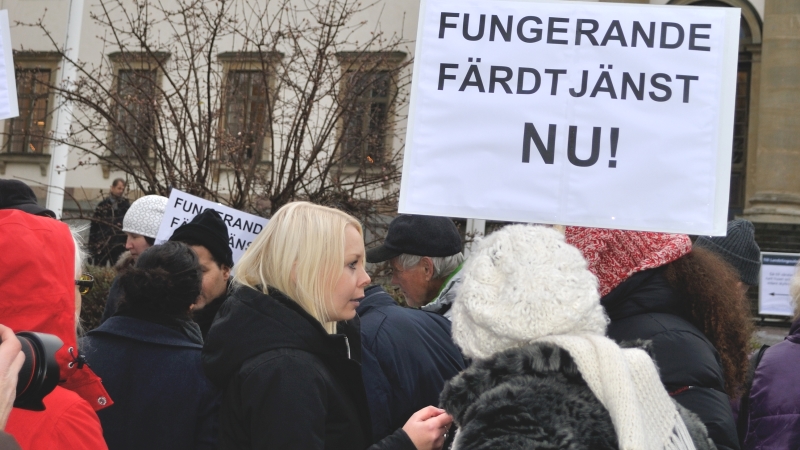 Folksamling framför landstingshuset och plakat med texten "Funderande färdtjänst NU!" 