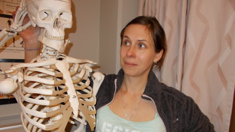 Kvinna med brunt hår invid ett skelett som gör honör.