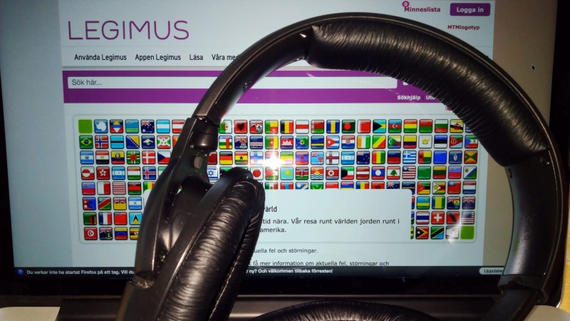 Stora hörlurar ligger framför en uppfälld laptop, där man skymtar Legimus webbplats.