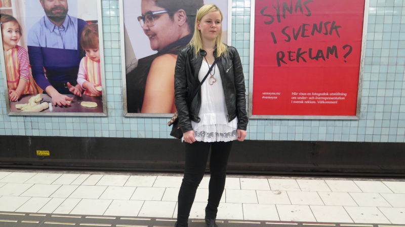En kvinna som står på en tunnelbaneperrong med utställningen bakom sig.