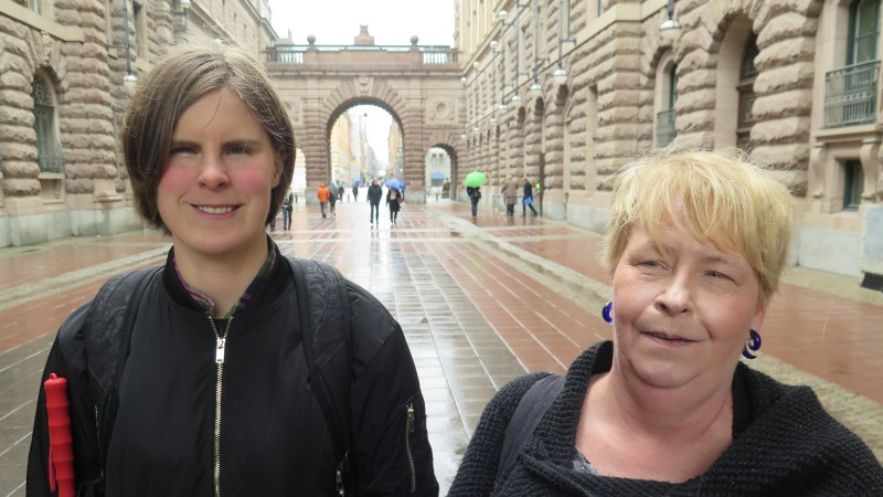 Ida Östlund och SRF:s Lena Ridemar i halvfigur i regn framför riksdagshuset.
