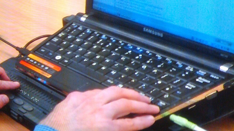 Händer på punktskriftstangenter framför en laptopskärm. 