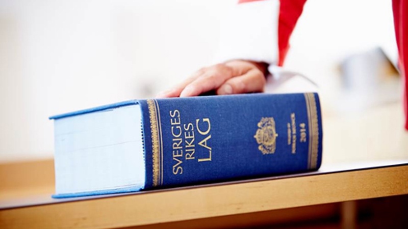 Svensk lagbok i blått ligger på ett bord, en hand vilar på boken