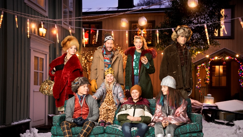Skådespelarna från SVT:s julkalender samlade i och bakom en soffa på en julbelyst innergård.