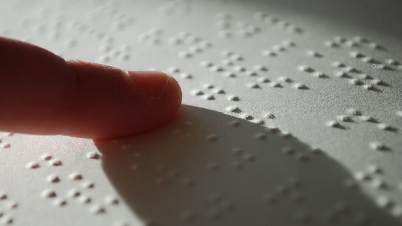 Ett pekfinger som dras över ett ark med punktskrift och kastar en stor skugga. Foto: Stefan Malmesjö/Flickr