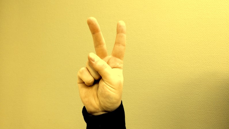 En hand, fingrarna gör V-tecken. Pek och långfinger hålls upp som i ett V
