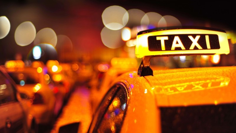 Närbild tak på en gul taxi med taxiskylt. Åker i stad, natt.