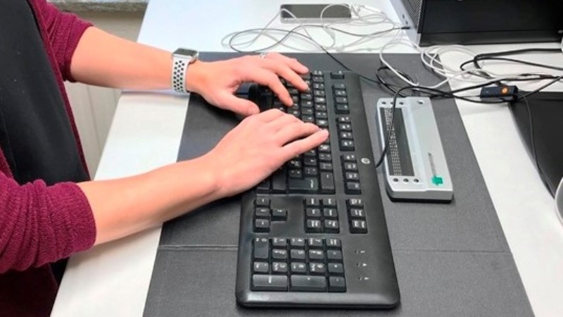 En kvinna skriver med båda händerna på ett tangentbord. Punkskriftsdisplay vid sidan