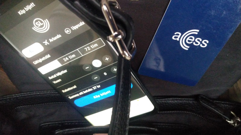 En smart telefon med SL-appens biljettfunktion öppen sticker upp ur en handväska intill ett mörkblått SL-kort med texten Acess.