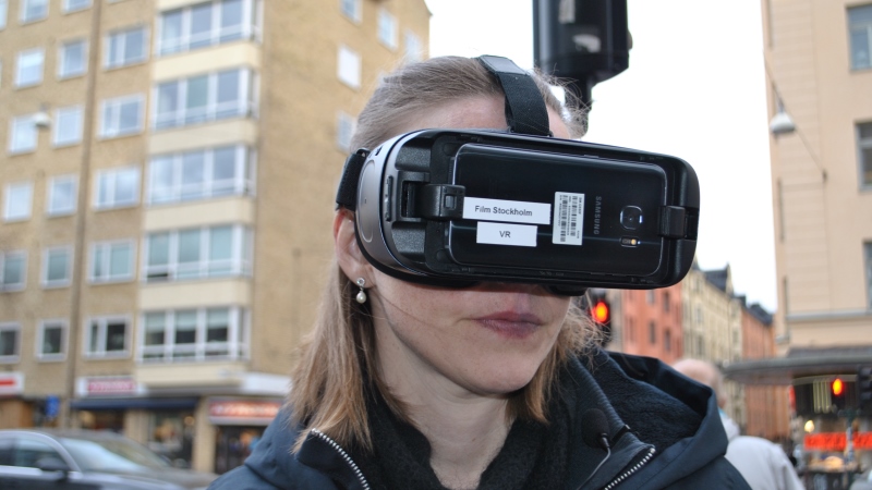 En kvinna i gatumiljö med större delen av ansiktet täckt av stora svarta VR-glasögon