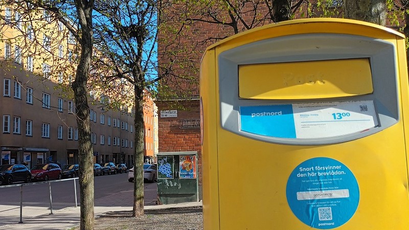 En gul brevlåda i gatumiljö med en blå rund lapp på där det står bland annat ”Snart försvinner den här brevlådan”.