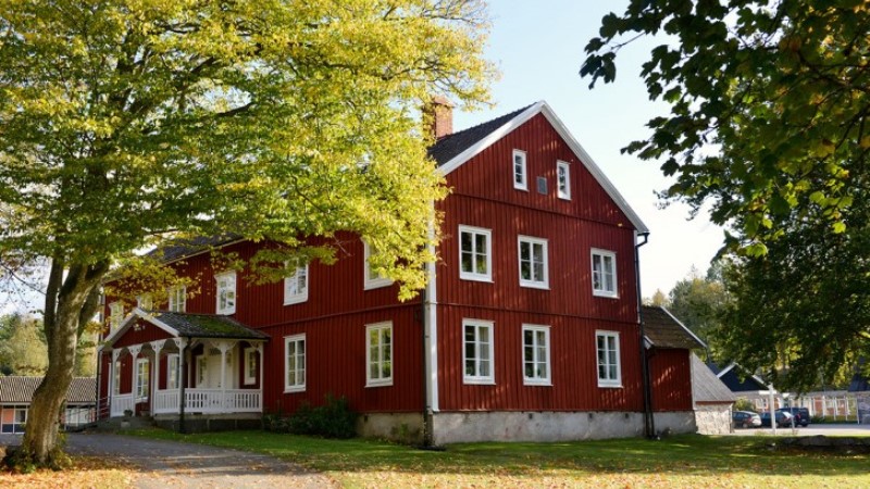 Glimåkra folkhögskola. En stor röd byggnad med vita knutar i lantlig lummig miljö.
