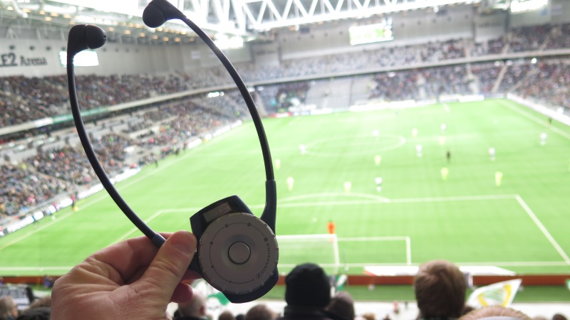 Syntolkningsmottagare med hörlurar, fotbollsplan i bakgrunden