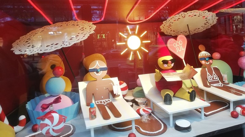 Syns i ett skyltfönster: Tre figurer solar sig inuti en ugn. Två pepparkakor och en lussebulle med en röd tomteluva.