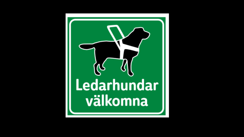 Grön skylt med svart ledarhund med vit sele, text: Ledarhundar välkomna