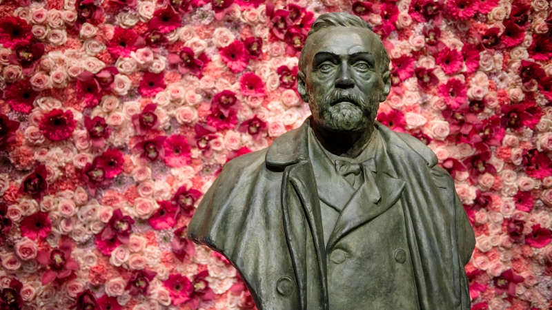 Byst av Alfred Nobel, står framför vägg dekorerad med röda, rosa rosor