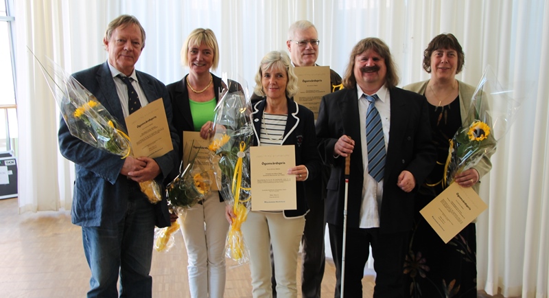 Fem pristagare fotas tillsammans med Håkan Thomsson, ordförande i SRF. De håller blommor och ler.