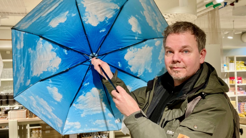 Man håller i ett uppslaget paraply som har ett tryck på insidan av ljusblå himmel med vita moln.