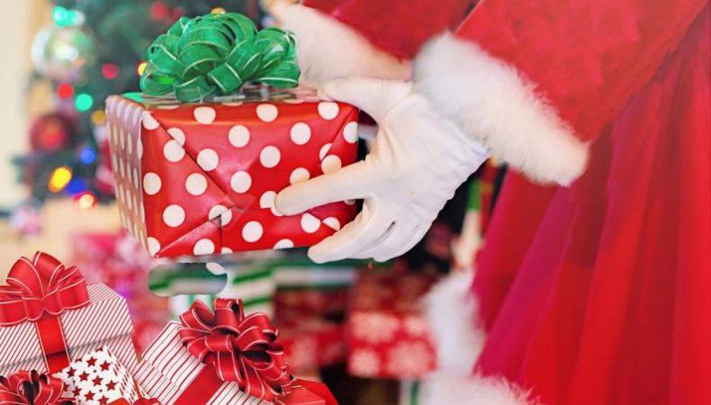 Julpaket lyfts upp ur säck av händer i vita handskar, röd tomtedräkt skymtar.
