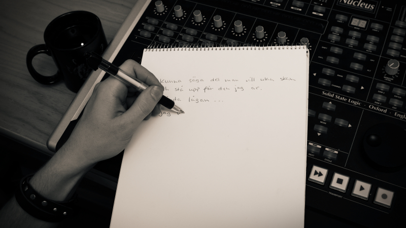 En hand som skriver i ett anteckningsblock. Bredvid står en kaffekopp.