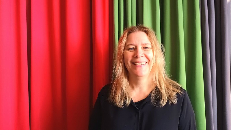 Christina Tånnander, en blond medelålders kvinna med medellångt hår nedanför axlarna. Hon står framför veckade draperier i tre olika färger: rött, grönt och grålila.