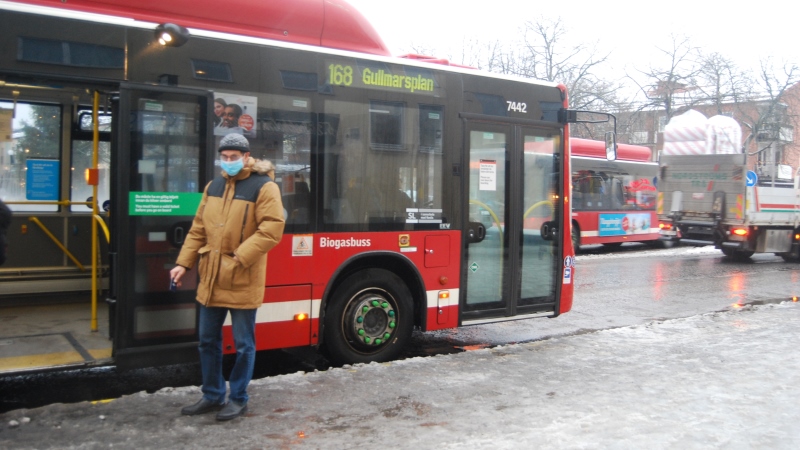 Man med blått munskydd står framför röd SL buss.