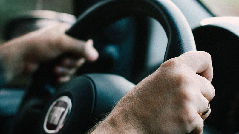 Närbild på ett par manshänder som håller i en ratt i en bil.